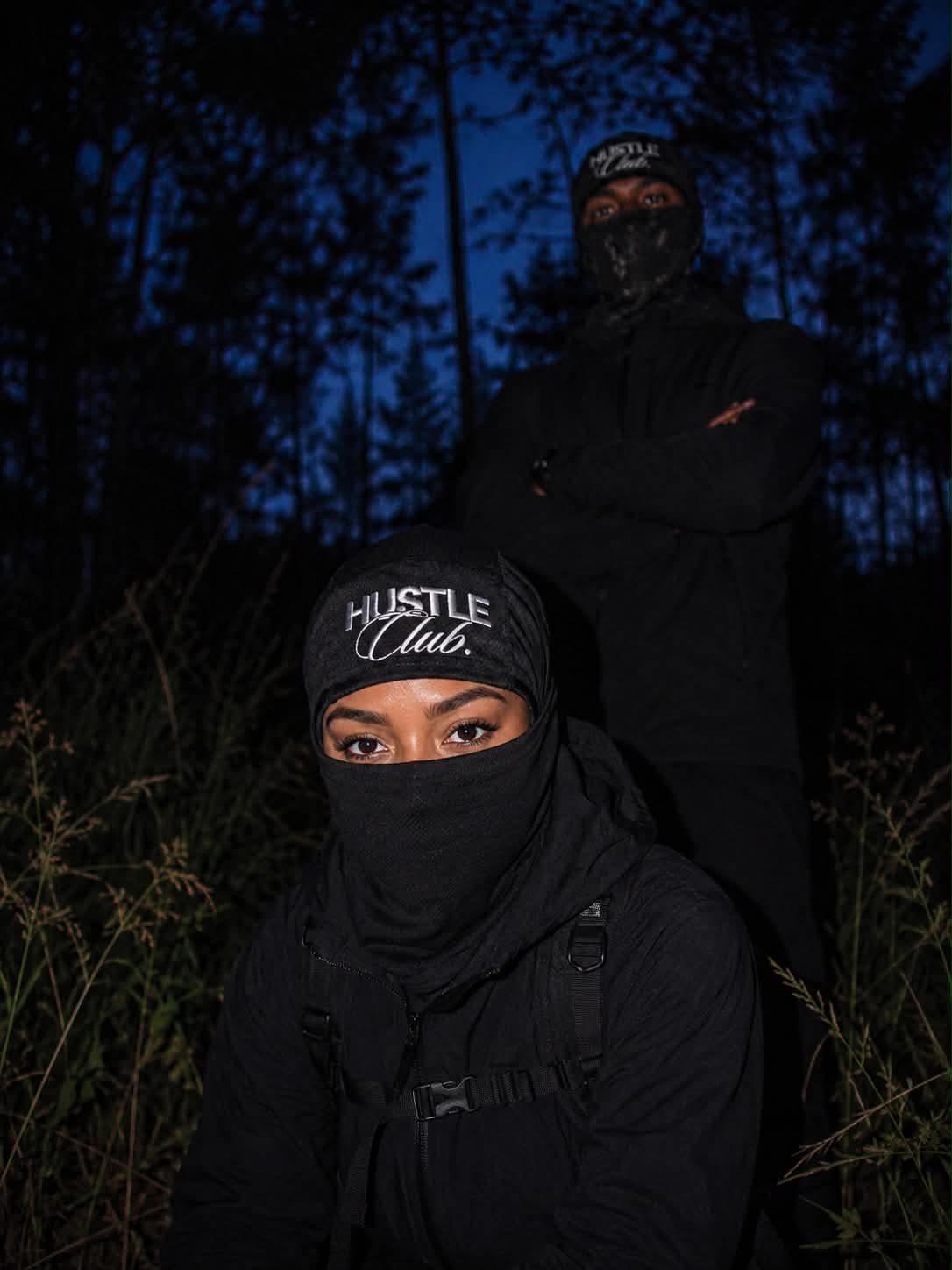 Deux modèles en cagoule noire dans les hautes herbes, à la nuit tombée.