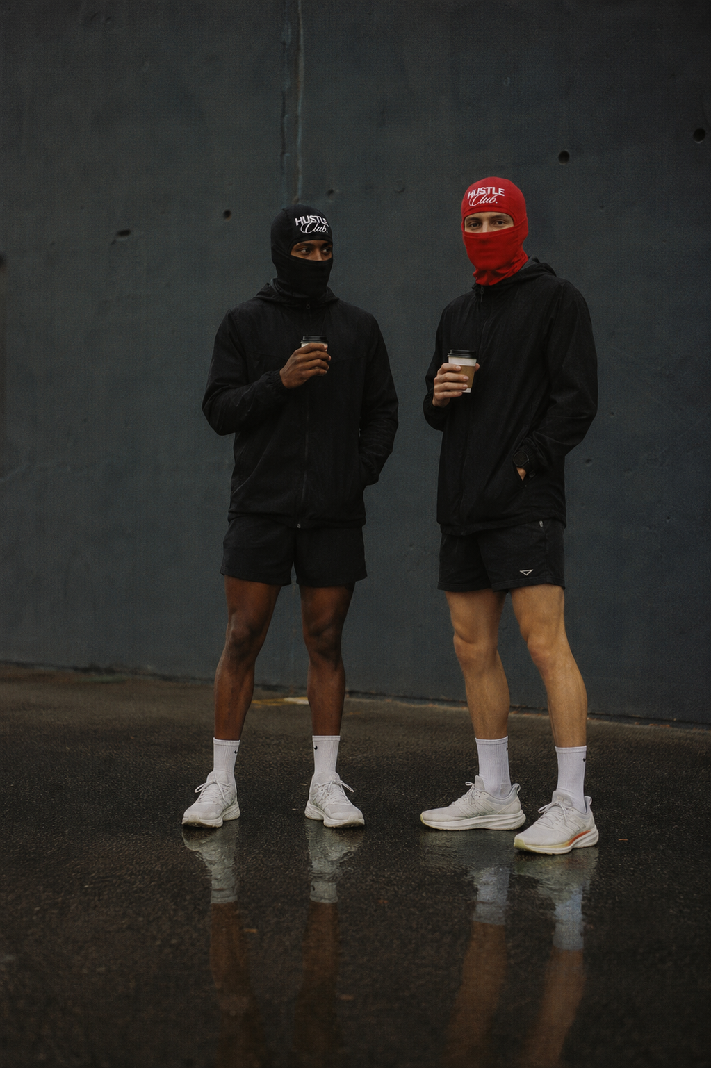 Deux modèles en cagoule noire et rouge, tenue running, café à la main sous la pluie.
