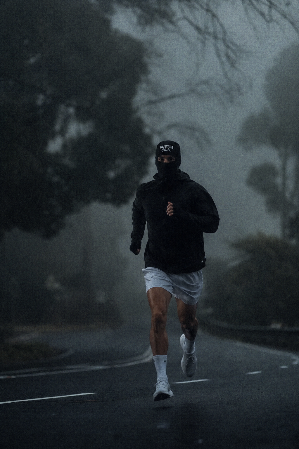 Modèle en cagoule noire courant sur une route brumeuse au petit matin.