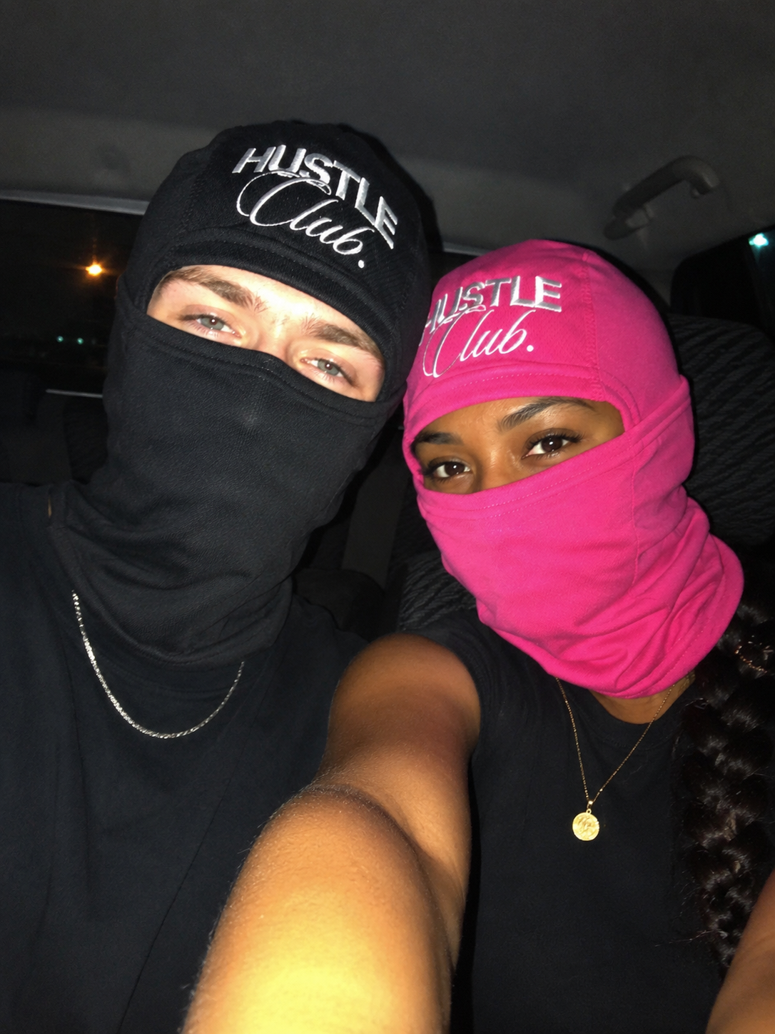 Couple en cagoules noire et rose dans une voiture, la nuit.