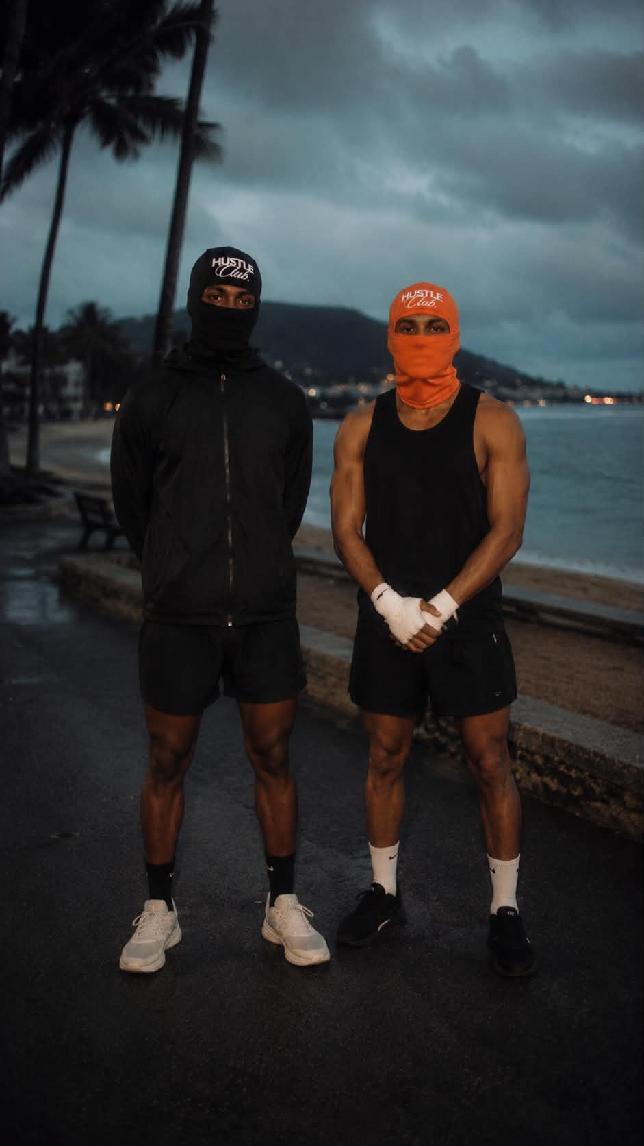 Deux modèles en cagoule noire et orange, tenue sportive au bord de mer à la tombée du jour.