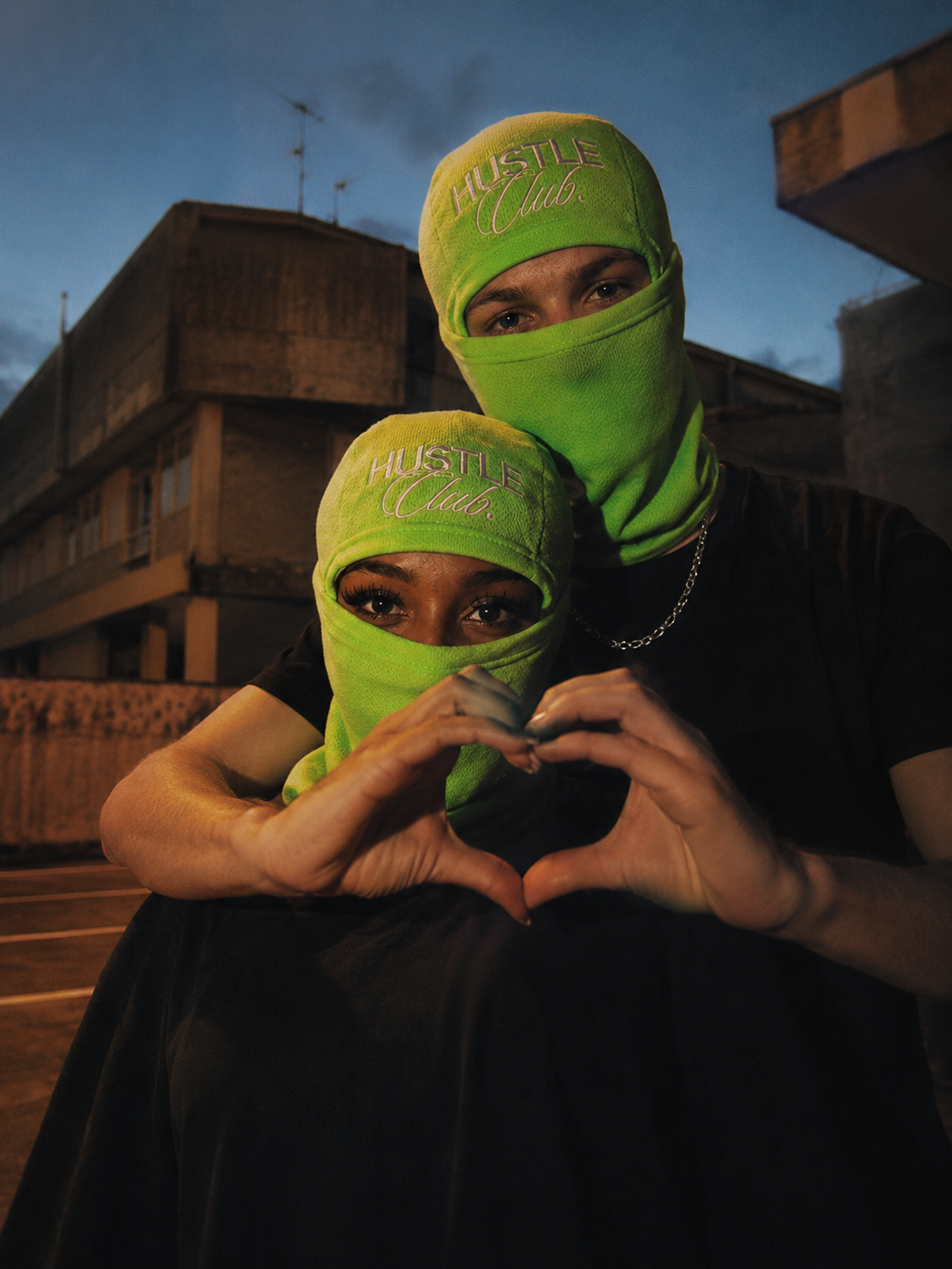 Couple en cagoules formant un cœur avec les mains au coucher du soleil.