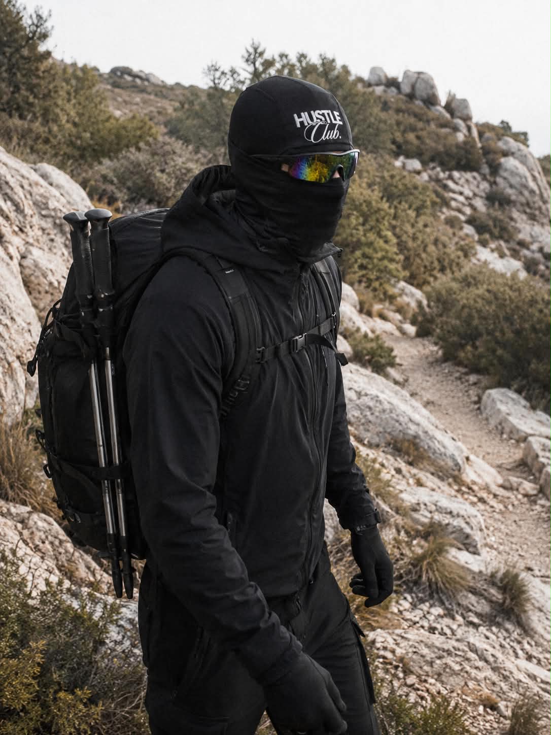 Modèle en cagoule noire et lunettes iridescentes en randonnée sur sentier rocheux.